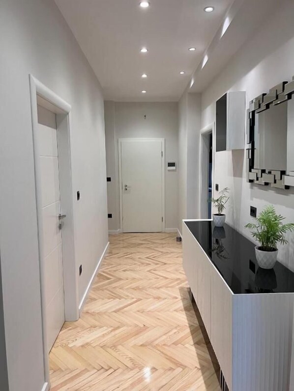 A modern hallway with a herringbone floor, a black reception desk, and a white door at the end. - Apartment Palm Tree (Dugi Rat)