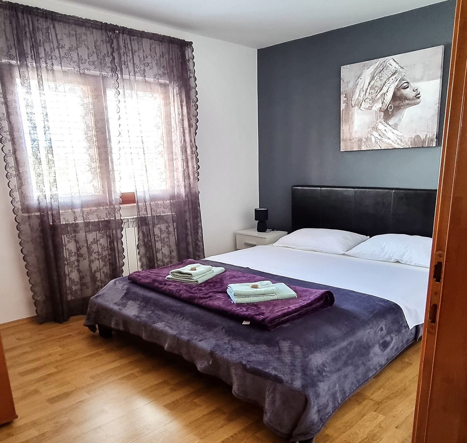 Une chambre à coucher avec un lit, une table de chevet, un tableau au mur et une fenêtre avec des rideaux.