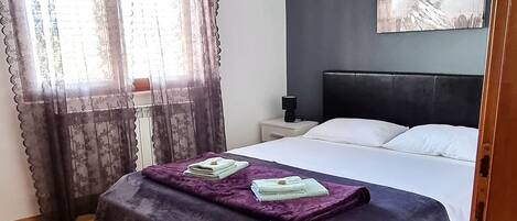 Une chambre à coucher avec un lit, une table de chevet, un tableau au mur et une fenêtre avec des rideaux.
