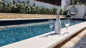 A poolside area with a stone wall, a hanging chair, and lounge chairs. - Apartments Villa Privlaka Relax (Privlaka)