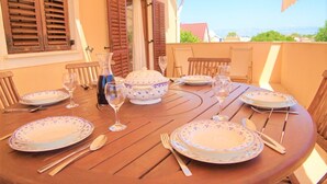 A round wooden table set for four with floral-patterned plates, cutlery, and wine glasses, overlooking a scenic view. - Apartments Villa Privlaka Relax (Privlaka)