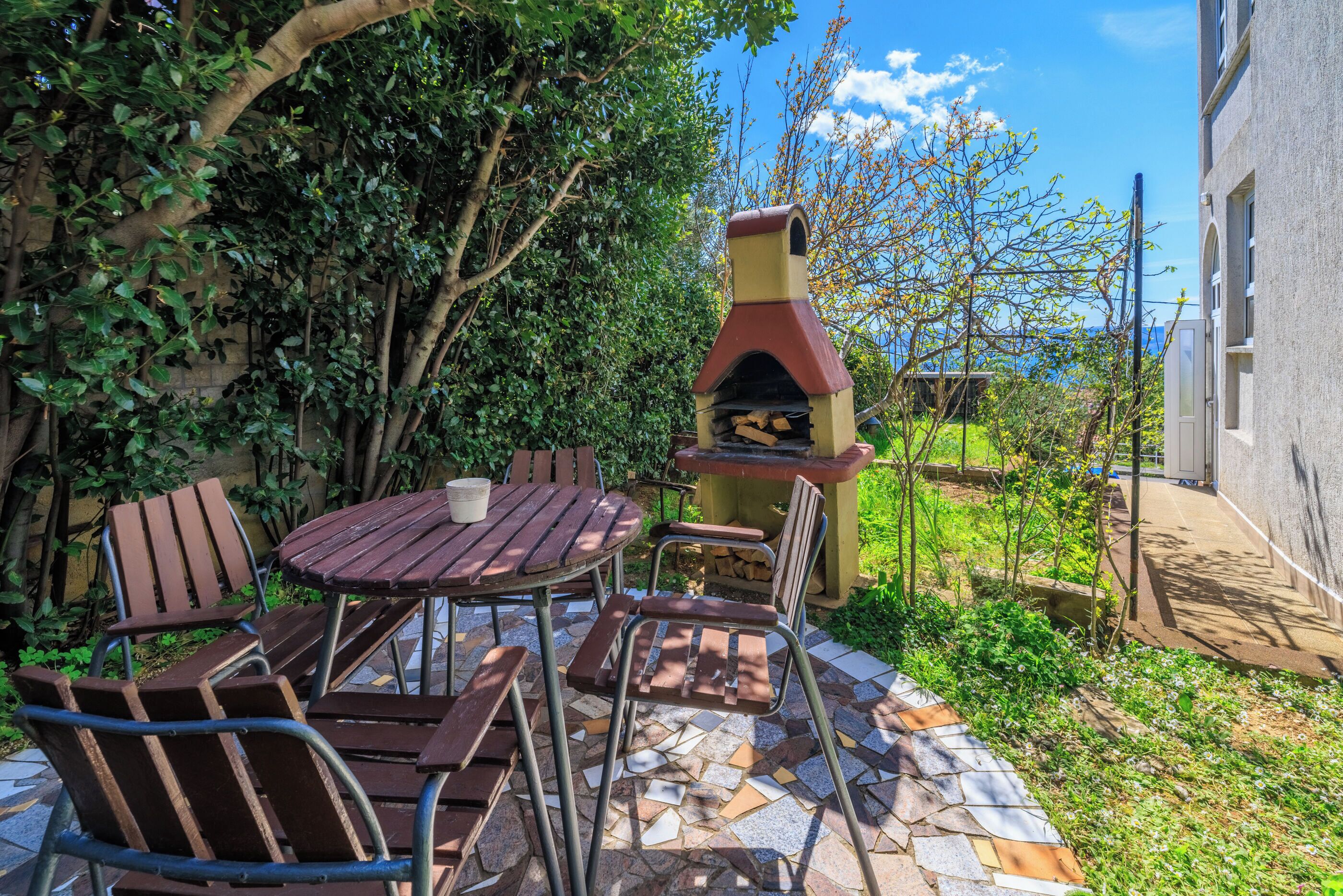 Une terrasse extérieure avec un sol carrelé en pierre, une table ronde en bois et des chaises en métal.