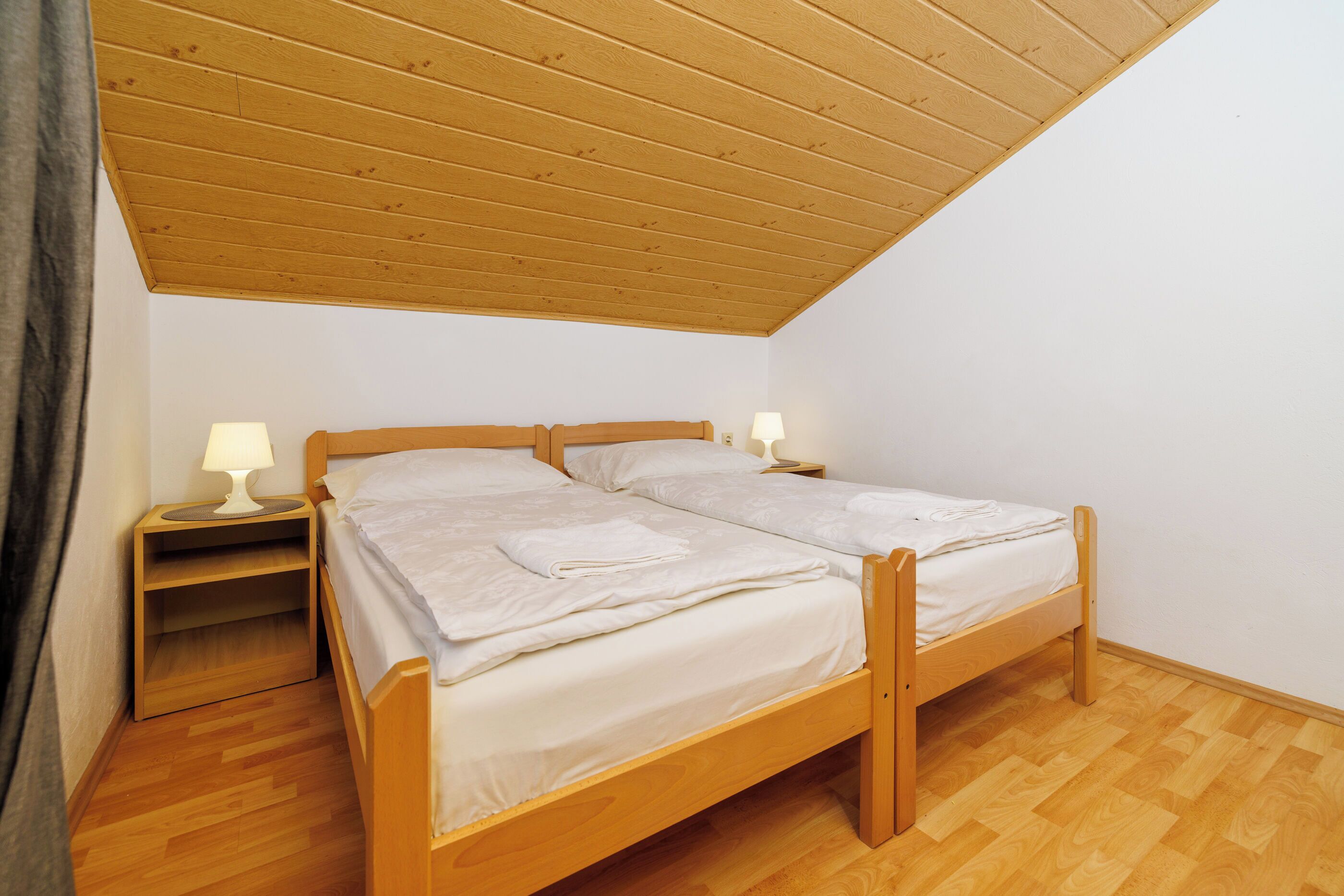 A room with a wooden bed, two bedside tables with lamps, and a wooden floor.