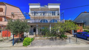 Un edificio a più piani con balconi, un'area di parcheggio e un'auto blu parcheggiata di fronte.
