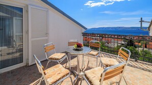 Un balcone con tavolo e sedie, vista sul mare e un edificio con facciata bianca.