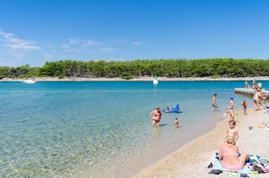 Een strand met helder water, mensen die zwemmen en zonnen, en een beboste kustlijn.