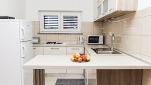 Une cuisine moderne avec des armoires blanches, un four à micro-ondes encastré, une cuisinière à gaz et un panier de fruits posé sur le comptoir.