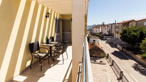 Un balcon avec une table et des chaises, donnant sur la rue, avec des bâtiments en arrière-plan.