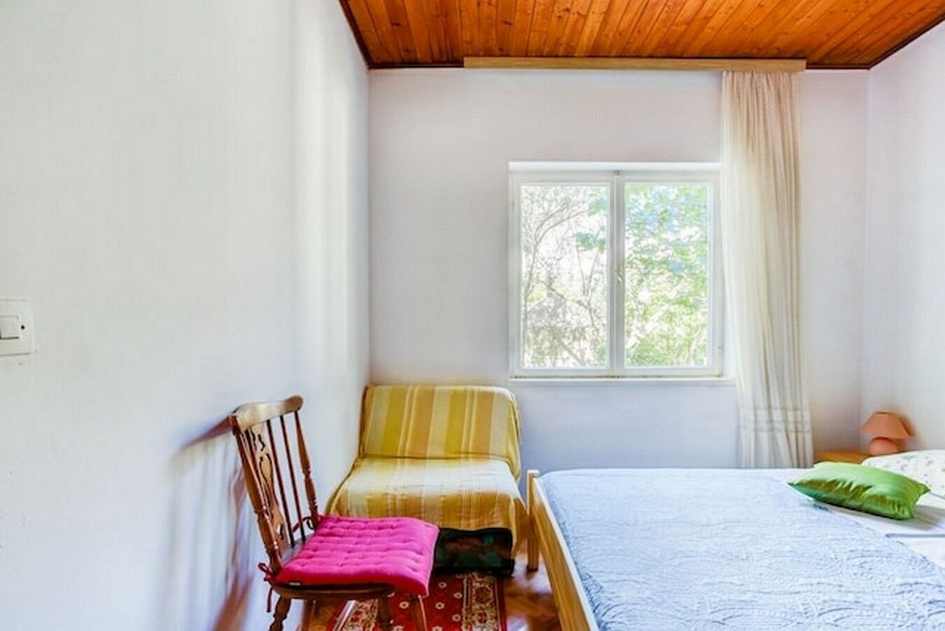 A bedroom with a bed, a chair, a window, and a lamp.