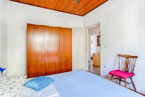 A bedroom with a wooden wardrobe, a bed with blue bedding, and a wooden chair with a pink cushion. - Apartments Katin Kutak (Sibenik)