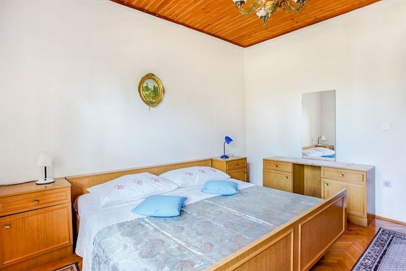 Een slaapkamer met een houten bed, nachtkastjes, een dressoir, een spiegel en een plafondlamp.