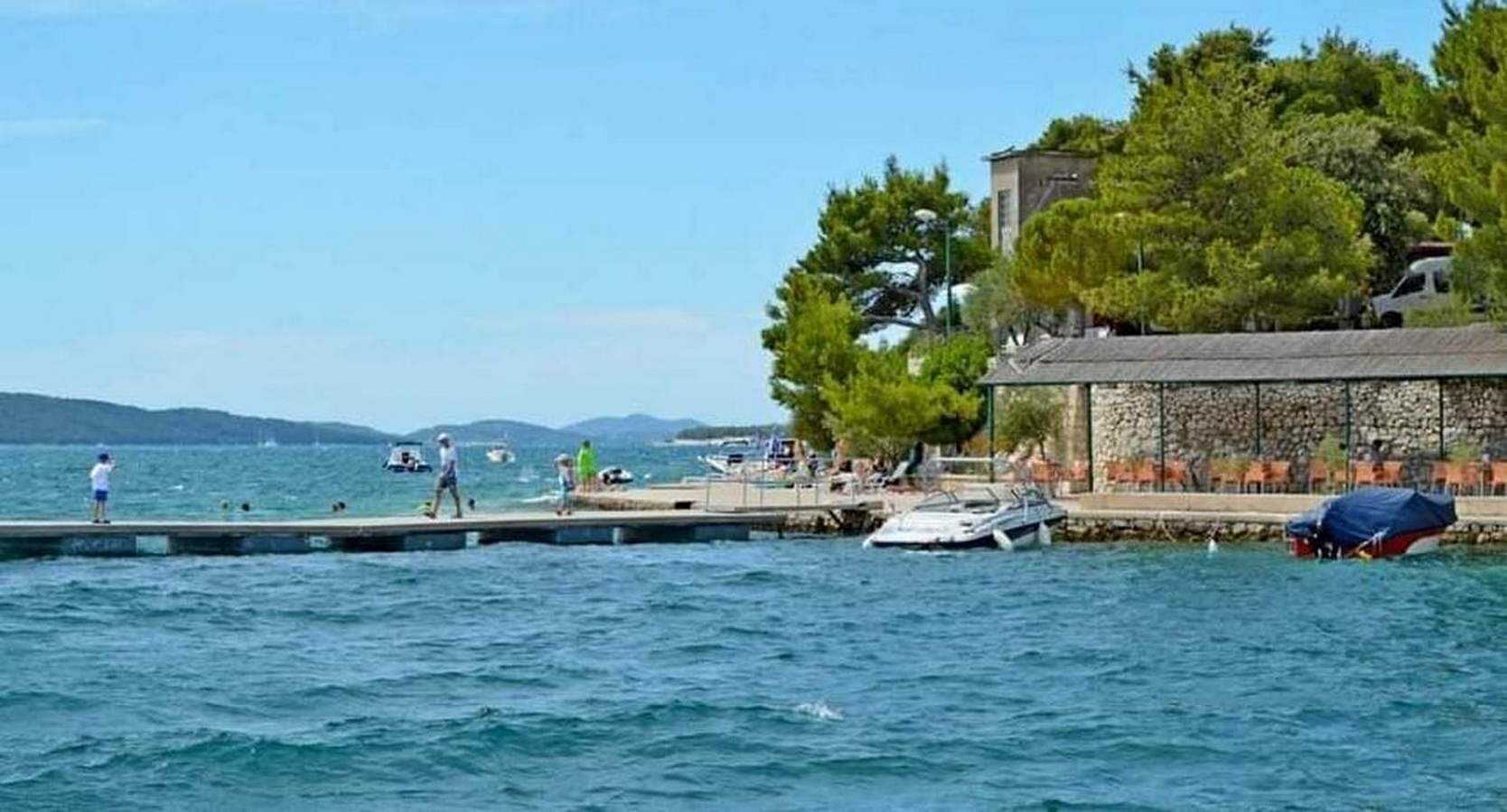 A waterfront scene with a pier, boats, and a building with outdoor seating.