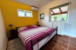 Un dormitorio con cama, mesita de noche, ventana y radiador.