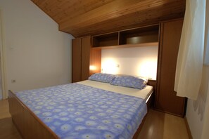 A bedroom with a bed, wooden headboard, and built-in shelving. - Apartment Ribaric (Rab)