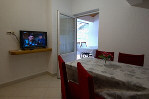 A dining area with a table set for two, a television mounted on the wall, and a door leading to an outdoor space. - Apartment Ribaric (Rab)