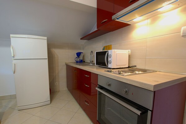 A compact kitchen with a refrigerator, microwave, oven, and sink. - Apartment Ribaric (Rab)