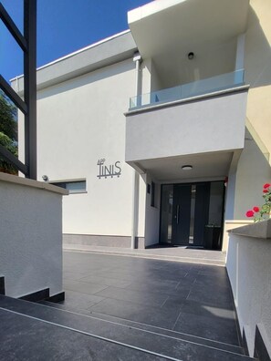 A modern building with a flat facade, a glass balcony, and a door with a sign above it. - House Tinis (Umag)