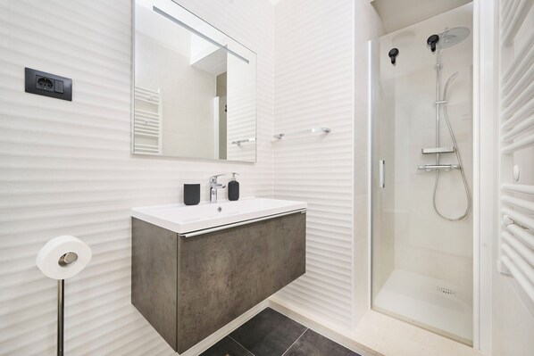A modern bathroom with a white vanity, a large mirror, a glass-enclosed shower, and a towel rack. - House Tinis (Umag)