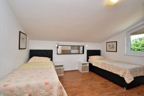 Une chambre avec deux lits simples, une petite table de chevet, une commode, un miroir et une fenêtre donnant sur un paysage verdoyant.