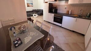 A modern kitchen with white cabinets, a microwave, and a stove. There is a dining table with a glass top and a woven placemat. - Apartment Pogi Srima (Vodice)