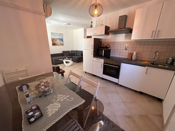 A modern kitchen with white cabinets, a microwave, and a stove. There is a dining table with a glass top and a woven placemat. - Apartment Pogi Srima (Vodice)