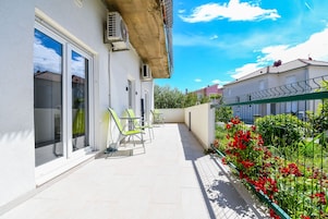 A balcony with a white tiled floor, green chairs, and a metal railing.