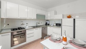 A modern kitchen with white cabinetry, stainless steel appliances, and a dining area with a table set for two. - Apartment Vista Olivo (Brtonigla)