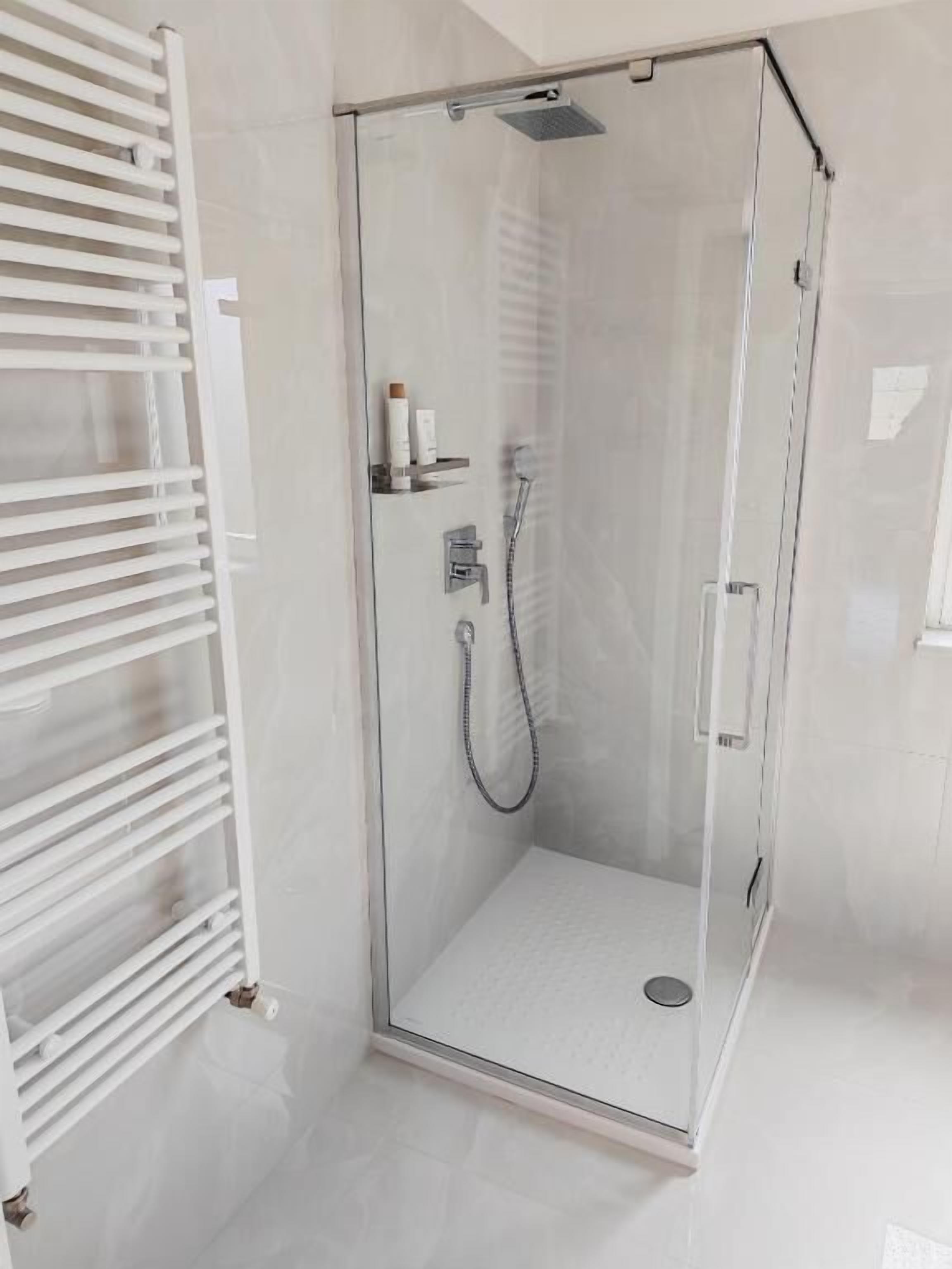 A glass-enclosed shower with a handheld showerhead and a wall-mounted faucet.