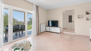 A spacious living room with a large sliding glass door leading to an outdoor area, a white cabinet with a flat-screen TV, and a door to another room. - Apartment Vista Olivo (Brtonigla)