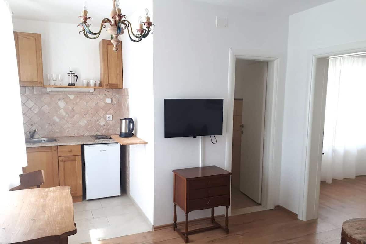 A compact kitchen with a dishwasher, a coffee maker, and a TV mounted on the wall.