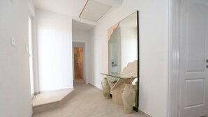 Un couloir avec un bureau dont le plateau est en verre, deux vases en céramique et un grand miroir.