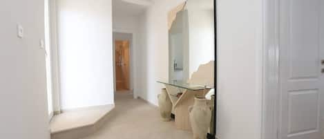Un couloir avec un bureau dont le plateau est en verre, deux vases en céramique et un grand miroir.