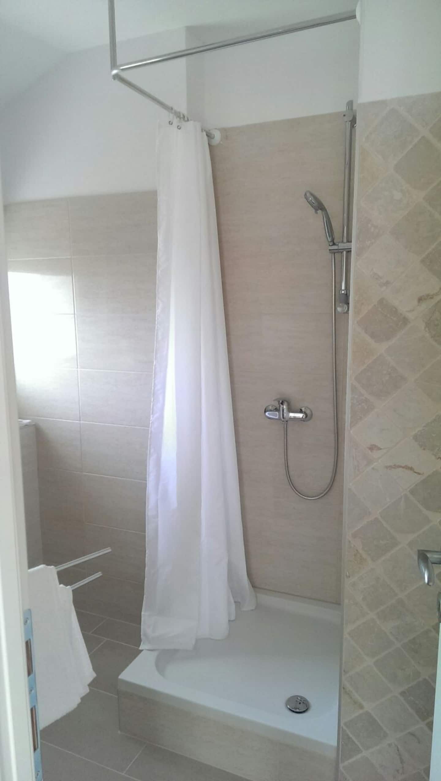 Un espace douche équipé d’un pommeau de douche, d’un rideau et d’un petit banc.