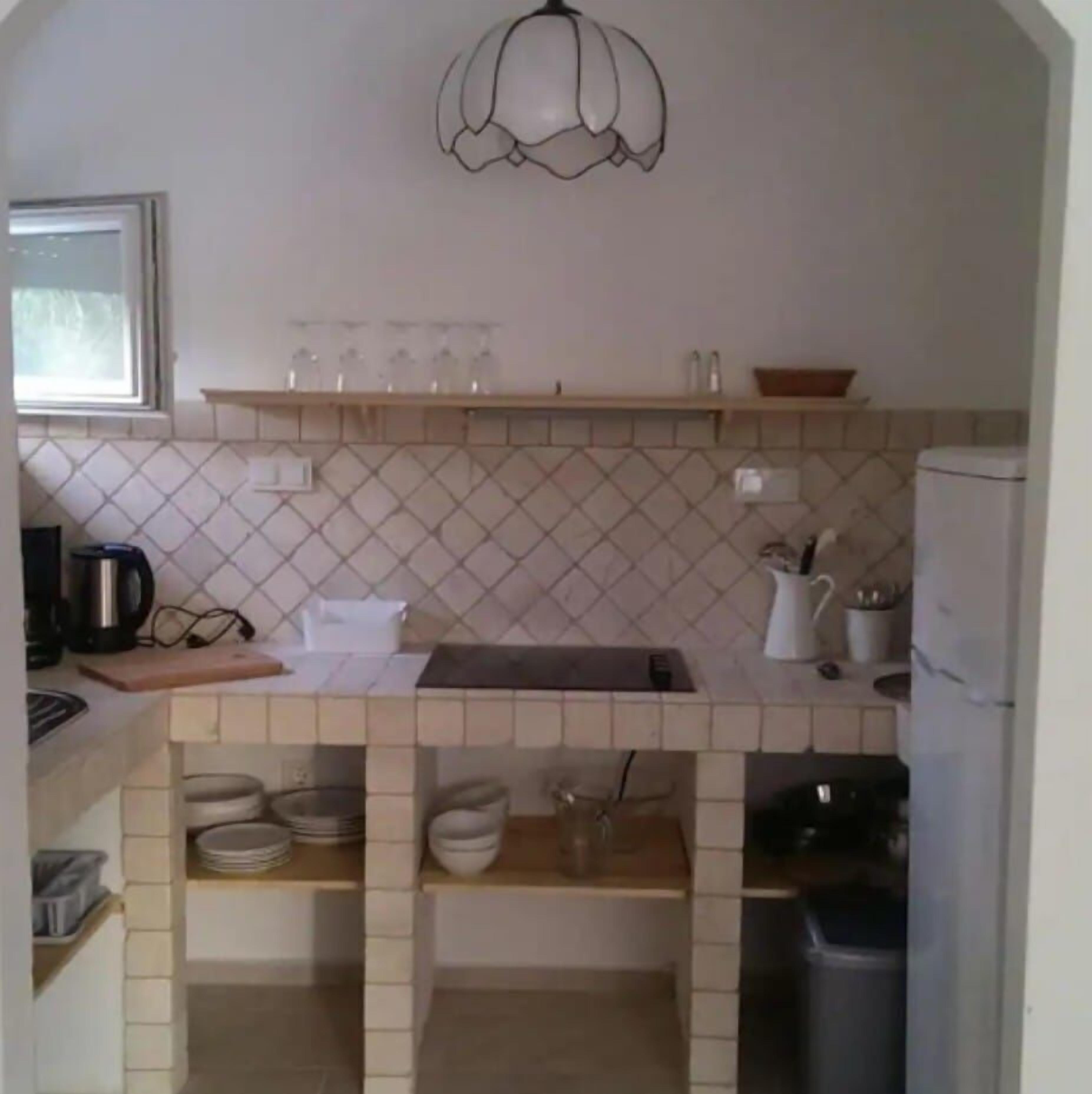 Una cocina con salpicadero de azulejos, un lámpara colgante y diversos electrodomésticos y utensilios.