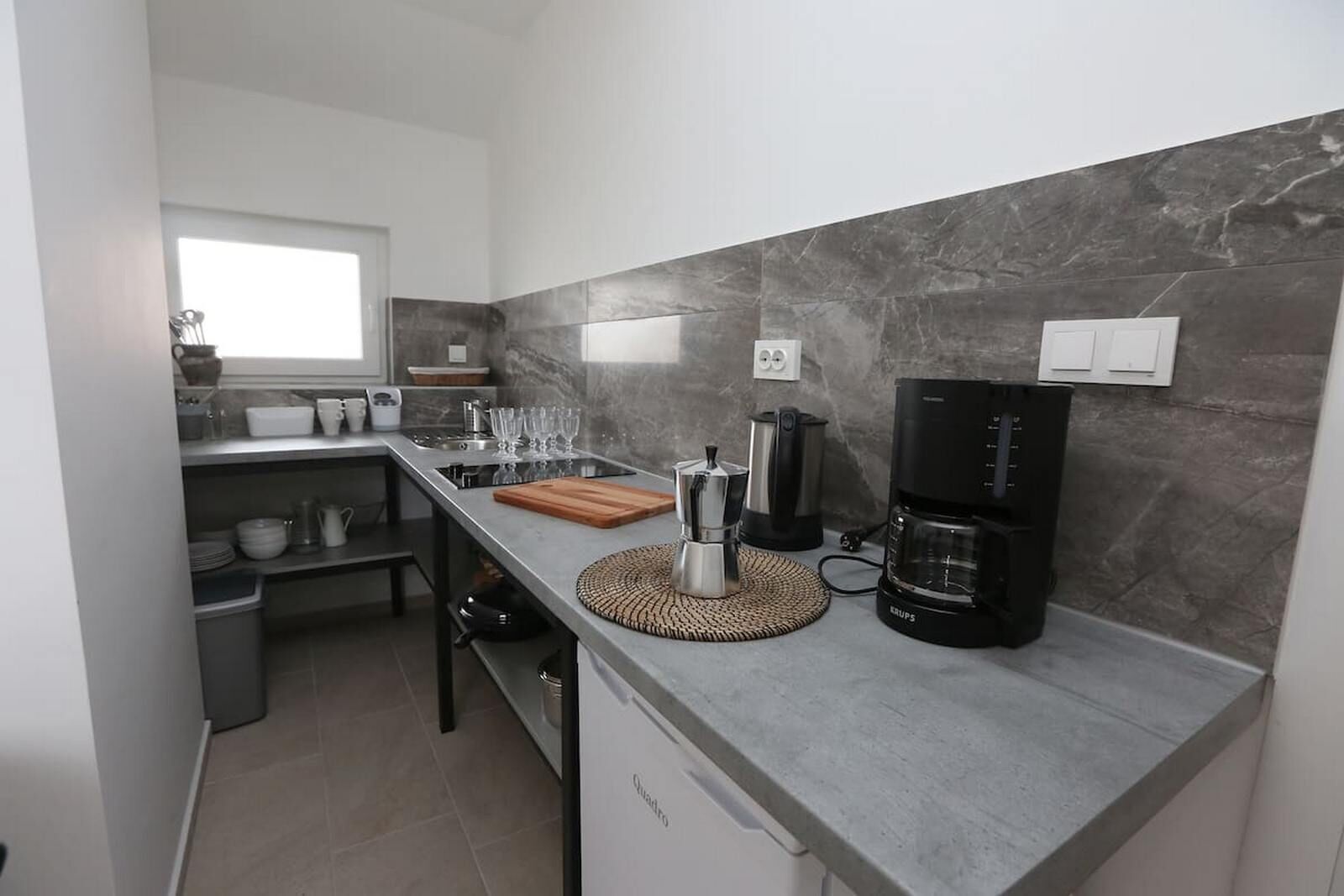 A compact kitchen with a grey countertop, a coffee maker, and a kettle.