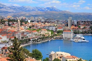 A coastal cityscape with a prominent tower, a marina with boats, and a mountainous backdrop. - Apartment Vesna (Split)