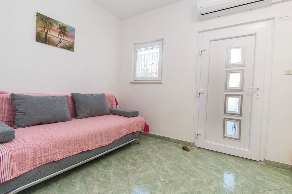 A room with a sofa, a door, a window, and an air conditioning unit.