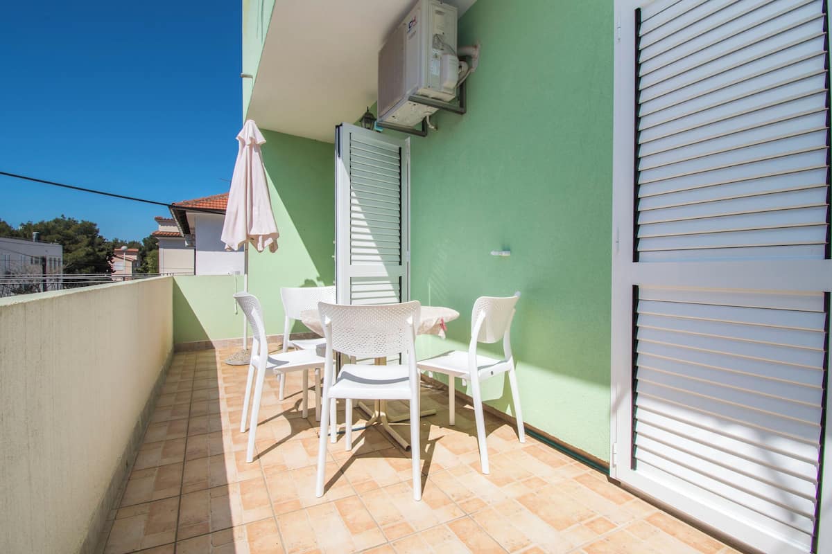 A balcony with a table and chairs, a closed white shutter, and an air conditioning unit.