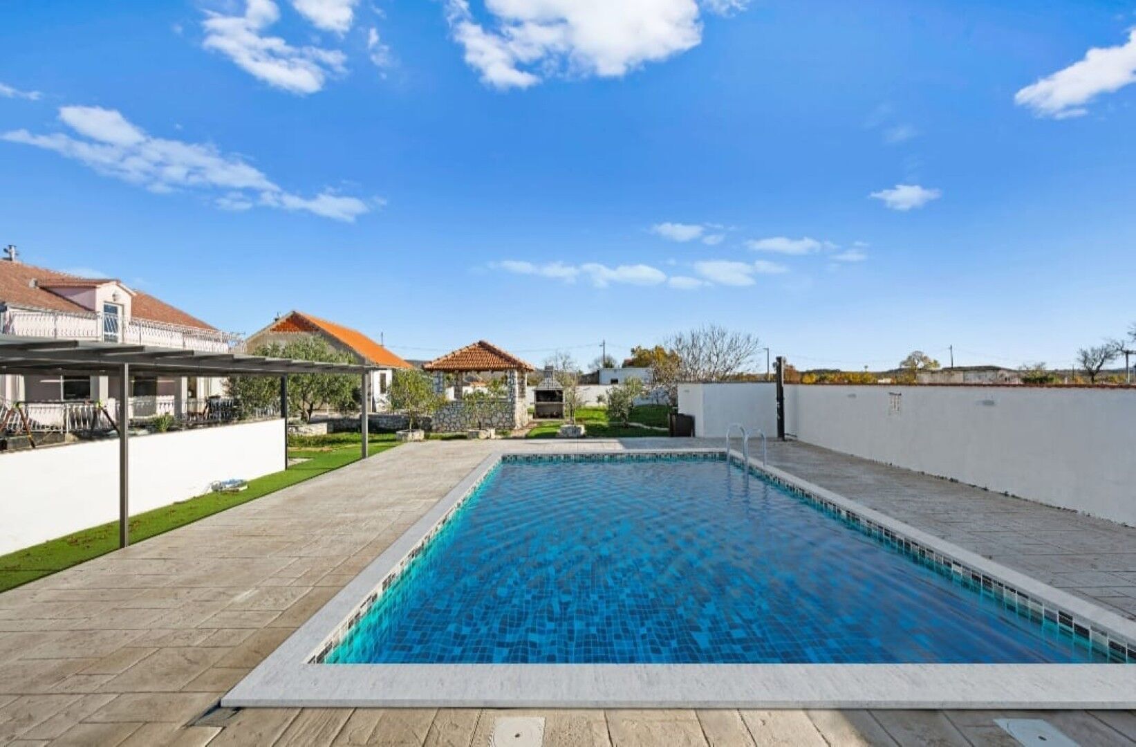 Una piscina rectangular amb superfície d'aigua blava cristal·lina, envoltada per un terra pavimentat i una paret blanca baixa.