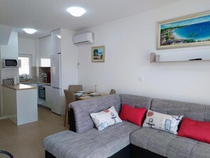Een moderne woonkamer met een grijze bank, rode kussens en een schilderij van een kustlandschap.