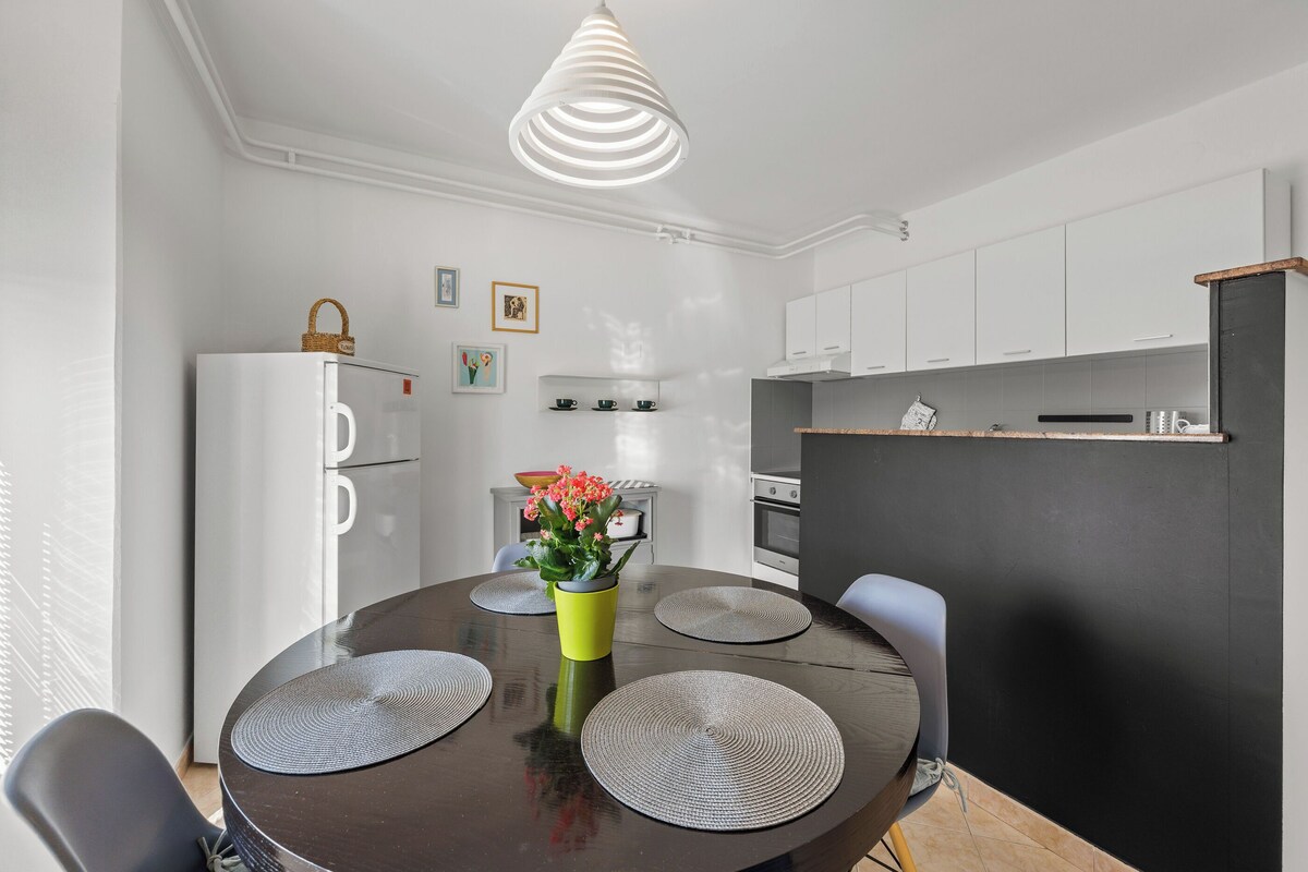 A modern kitchen with white cabinets, a black countertop, and a hanging light fixture.