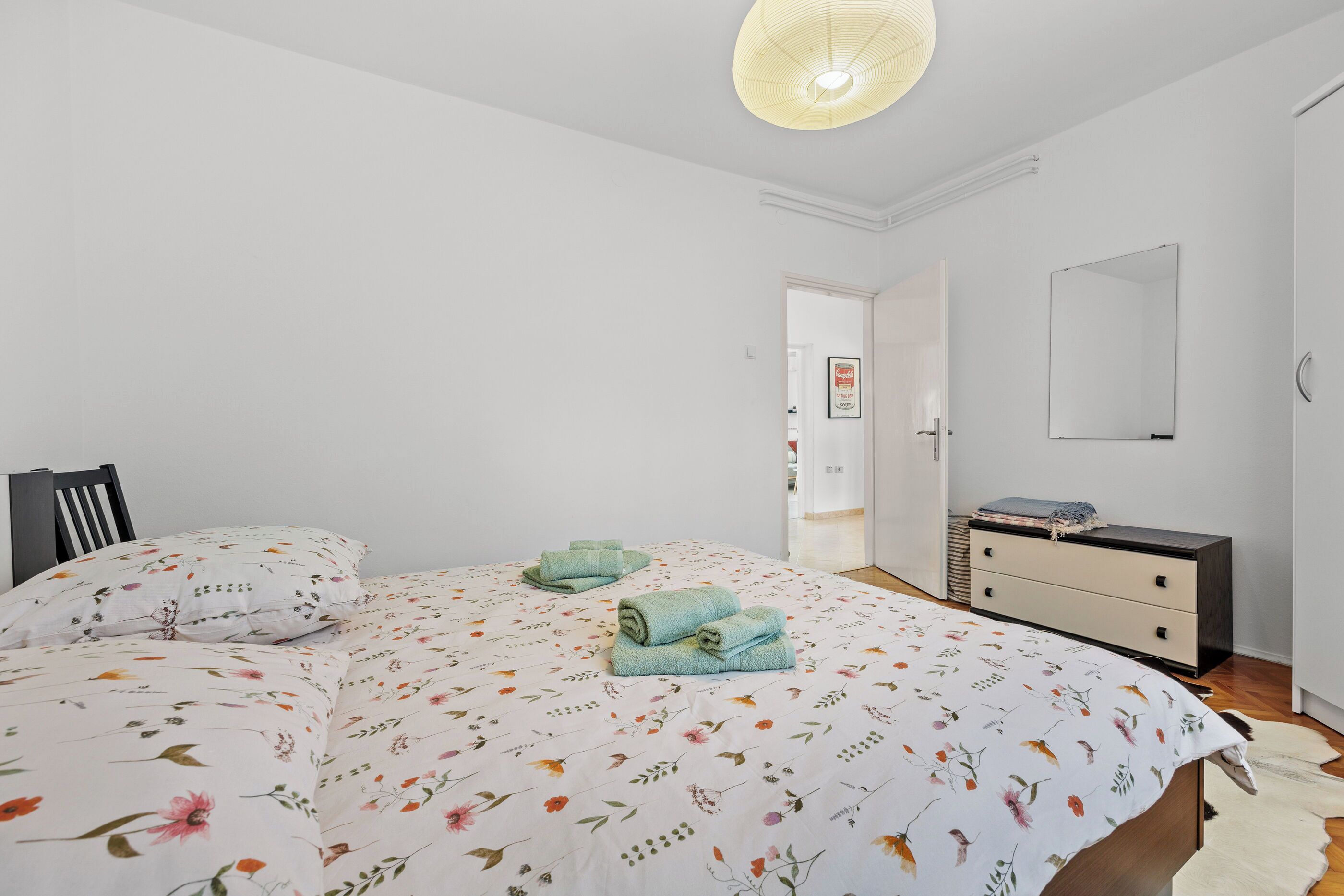 Ein Schlafzimmer mit Bett, Schminktisch, Spiegel und einer Tür zu einem anderen Raum.