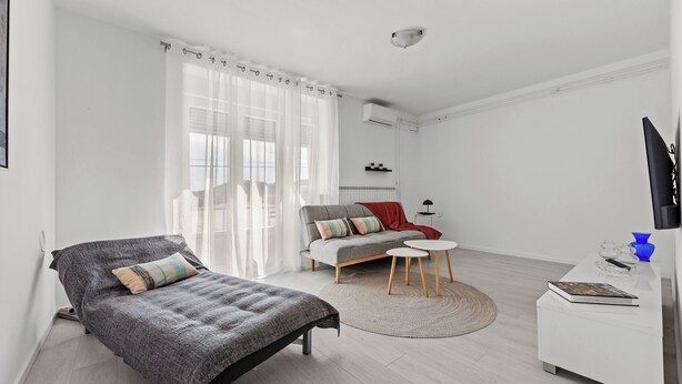 Ett modernt, minimalistiskt sovrum med en säng, en soffa, ett litet runt bord och en tv.