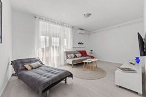 A modern, minimalist bedroom with a bed, a sofa, a small round table, and a TV. - Apartment Vinez (Labin)