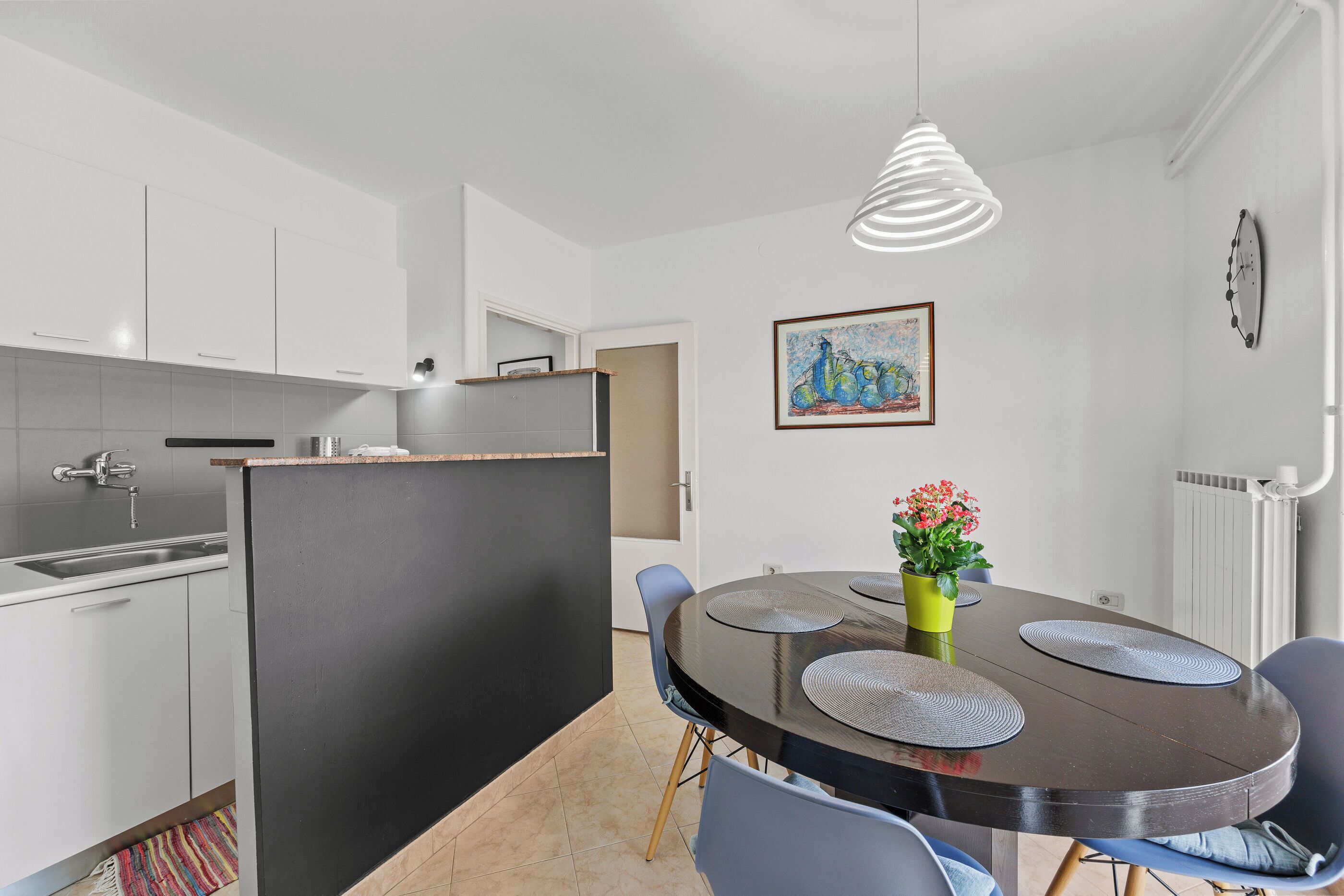 A modern kitchen with white cabinets, a black island, and a dining area with a round table and chairs.
