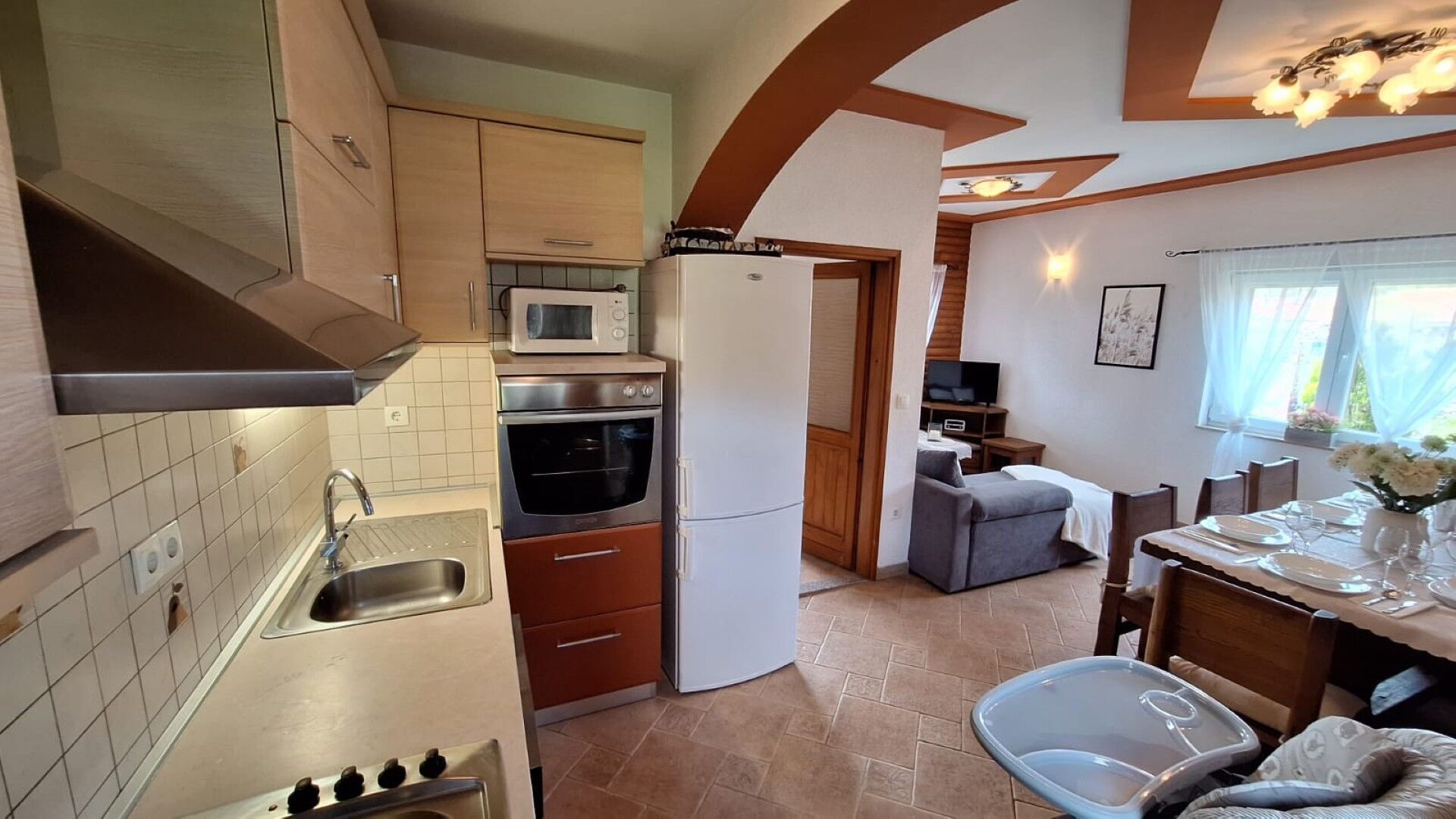 Eine kleine Küche mit Mikrowelle, Backofen und Kühlschrank. Es gibt eine Essecke mit Tisch für zwei Personen und ein Sofa.