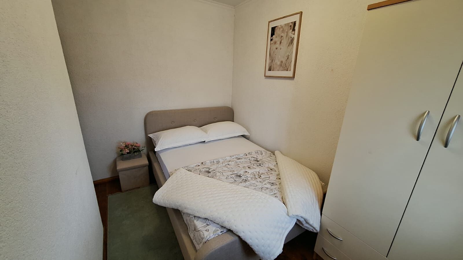 Una habitación pequeña con una cama individual, cabecera de madera, mesita de noche con lámpara y un armario con espejo.