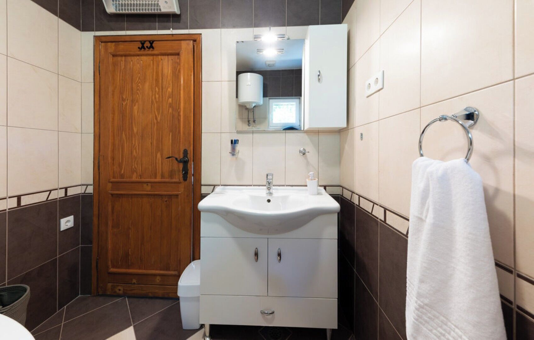 A bathroom with a wooden door, white sink, mirror, and towel rack.
