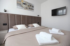 A modern hotel room with a large bed, a flat-screen TV mounted on the wall, and a decorative piece above the bed. - Apartment Ivana (Trogir)
