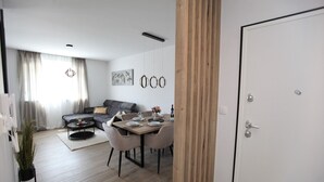 Un soggiorno moderno con un divano grigio, un tavolo da pranzo per quattro persone e una parete decorativa in legno.